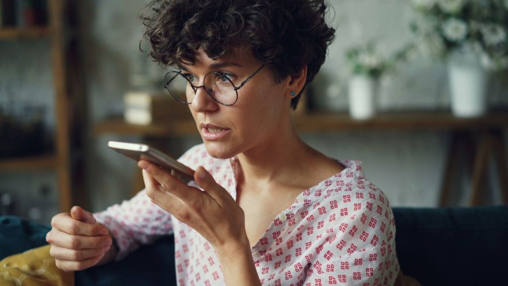 Mulher usa comando de voz no celular em casa.