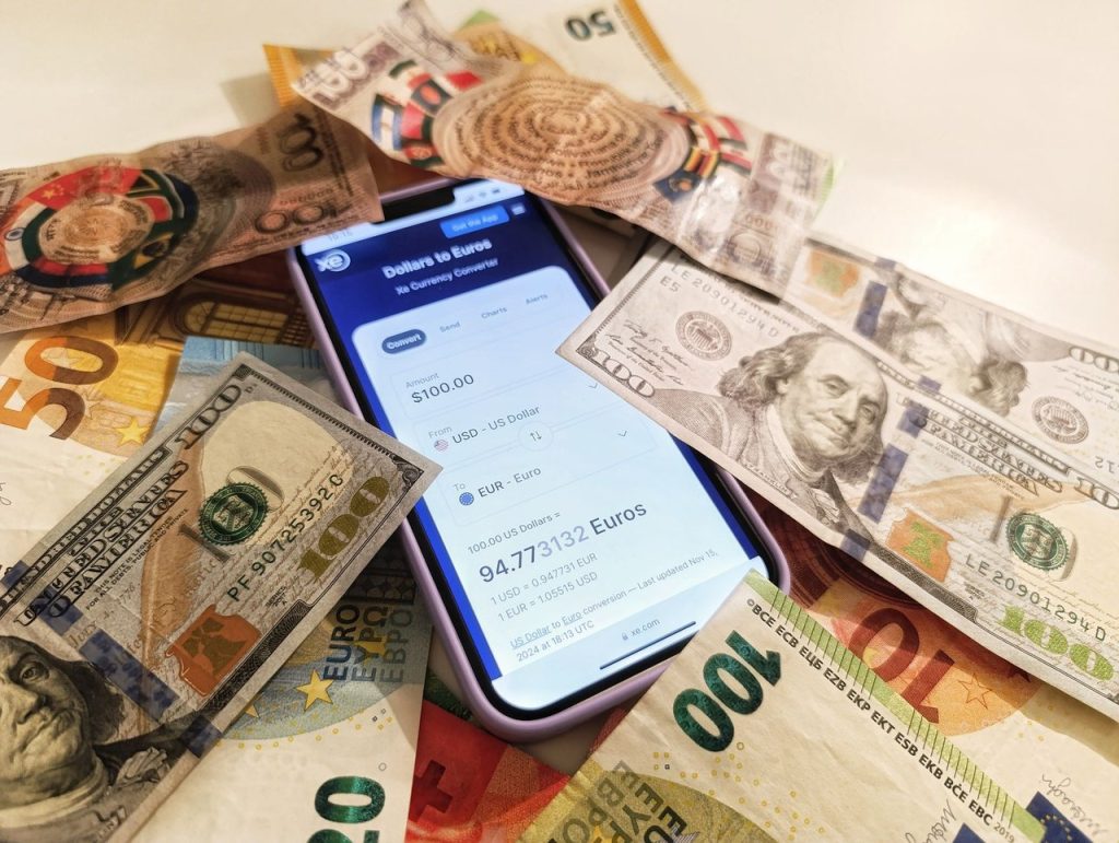 Smartphone exibindo um conversor de moedas cercado por notas de dólar e euro.
