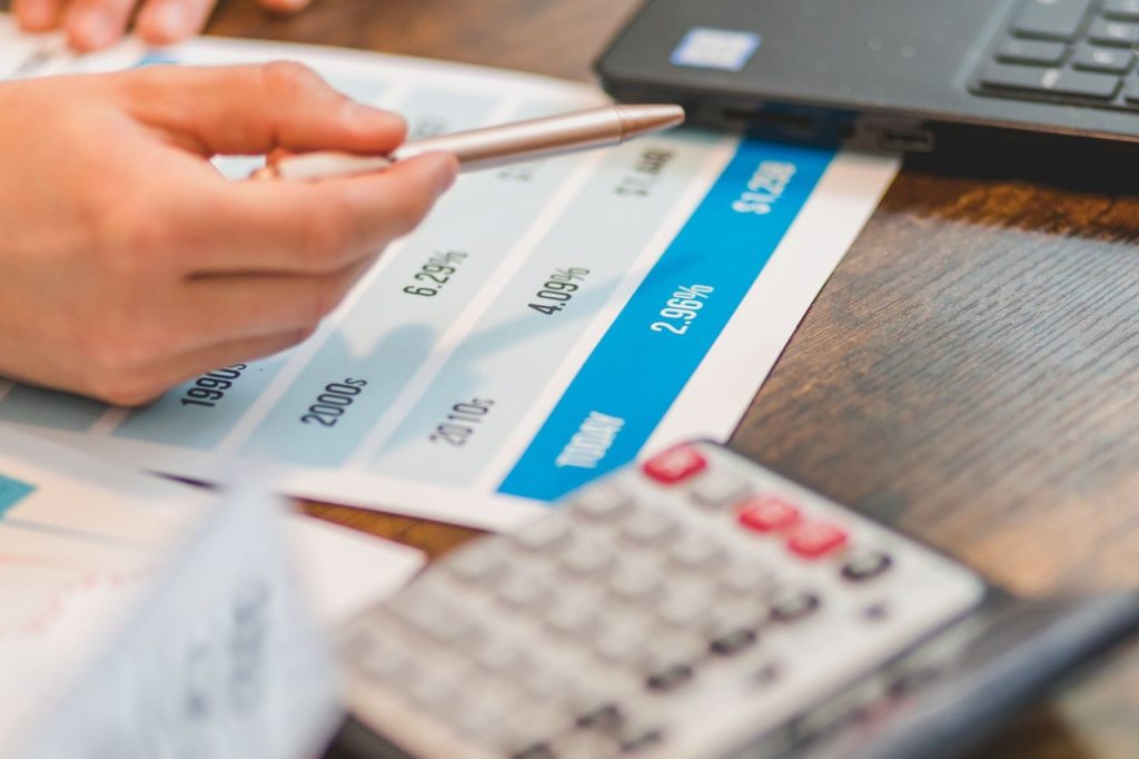 Mão usando uma caneta e uma calculadora para analisar taxas de juros em um gráfico.