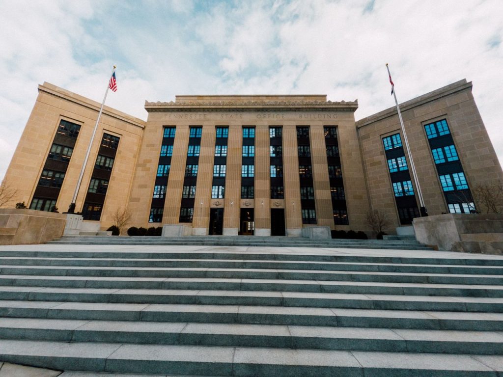 Exterior do prédio do Federal Reserve em Washington, com bandeiras dos Estados Unidos e uma escadaria sob céu nublado