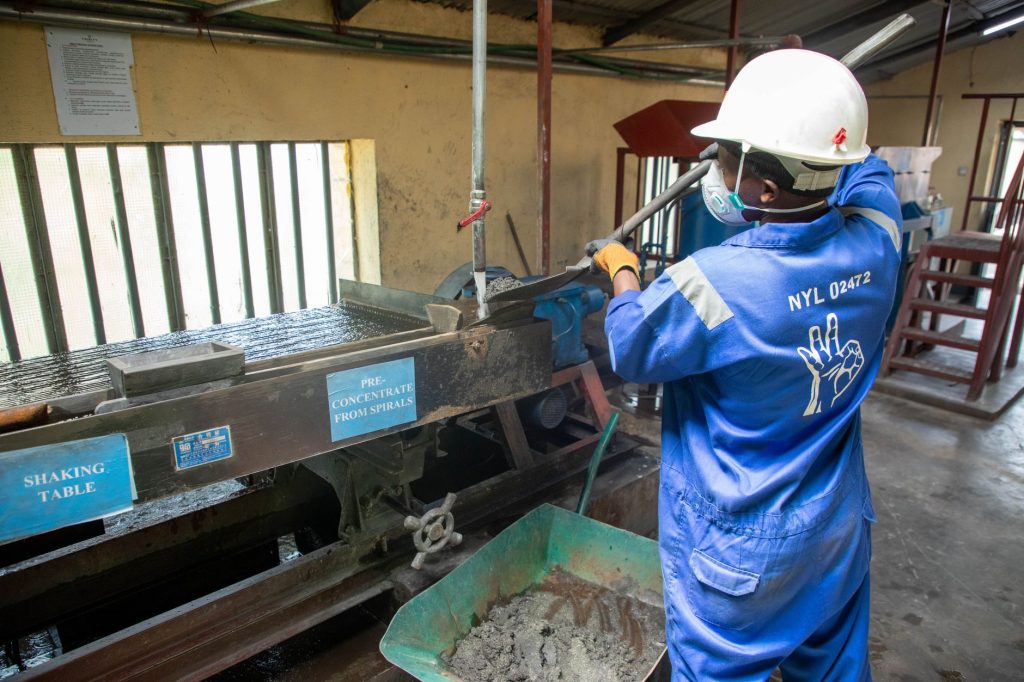 Brasil cria política para minerais críticos e prevê incentivos à industrialização e à mineração urbana Trabalhador usando uniforme azul opera uma mesa vibratória em uma unidade de processamento de minério.