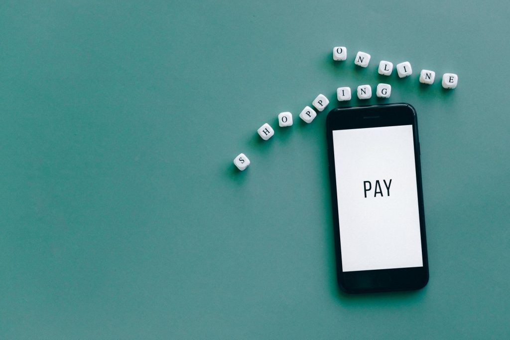 MP determina fim das bets no país e estabelece calendário para saques Smartphone exibindo a palavra “PAY”, cercado por dados que formam a expressão “online shopping”, sobre fundo azul.