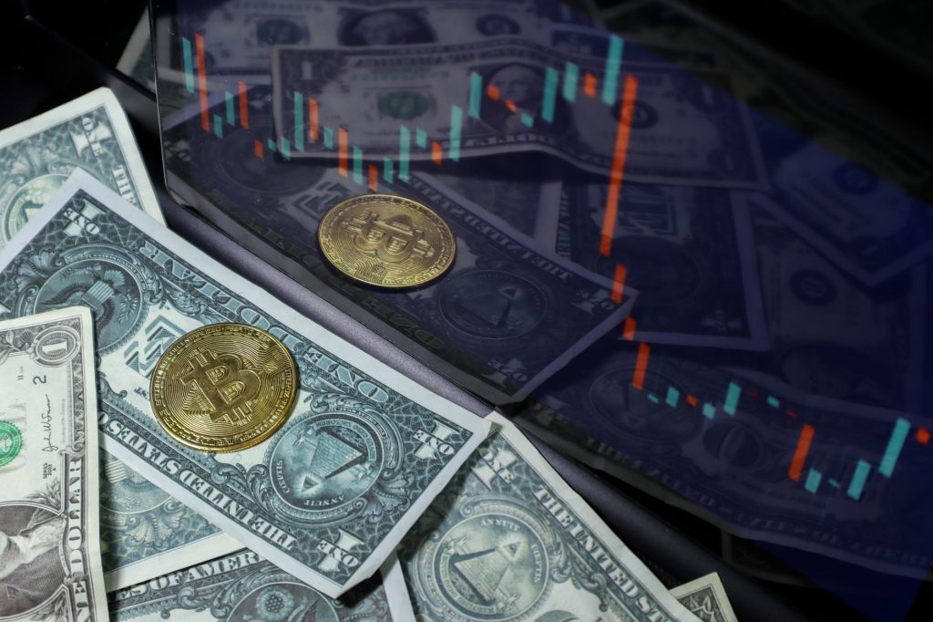 Moeda de criptomoeda sobre notas de dólar, com gráfico do mercado acionário ao fundo
